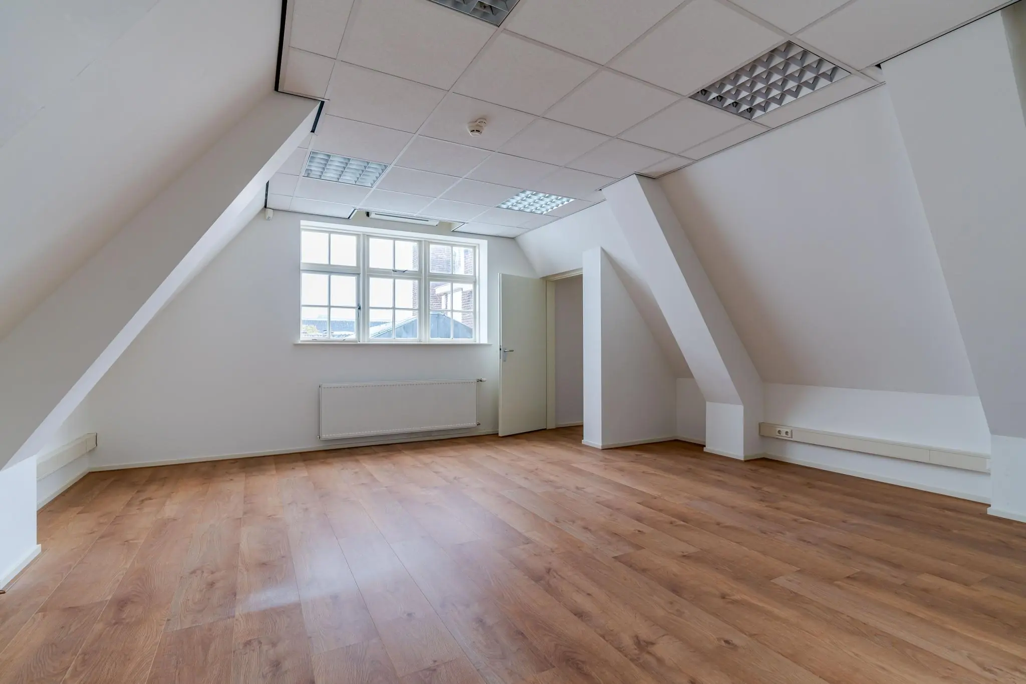 Lichte zolderruimte aan het Lange Voorhout met houten vloer, witgeschilderde muren en een groot raam.